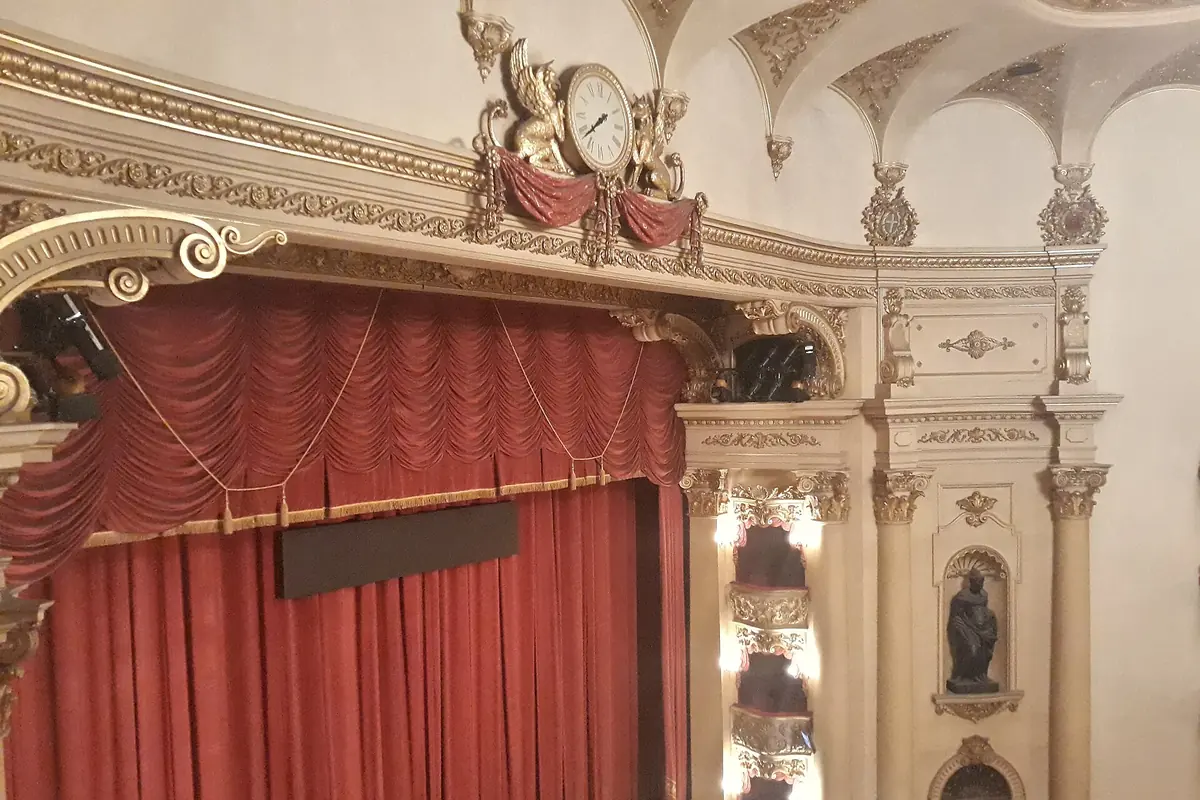 The stage of the Teatro Filarmonico, a red curtain beneath an ornate cream and gold arch