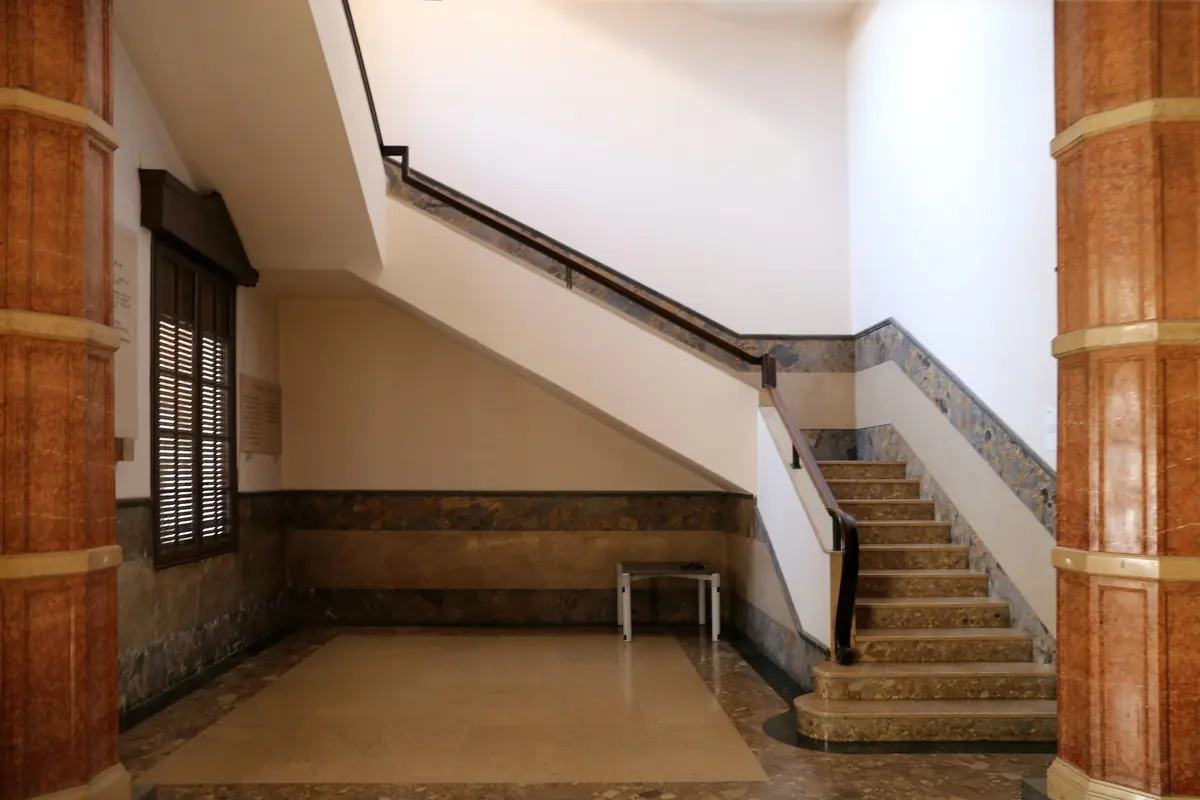 The stair hall of the palace, with a flight of marble steps, a slim handrail and red-brown columns